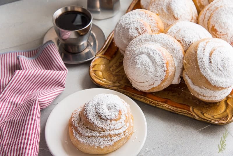 Mallorca Bread, a soft, sweet pastry dusted with powdered sugar, pairs perfectly with a cup of strong coffee.